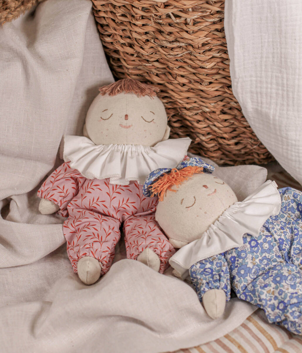 Two Little Lenni baby dolls, Emily and Liv, sleeping dressed in floral blue and pink overalls and with white ruffle collars around their necks.
