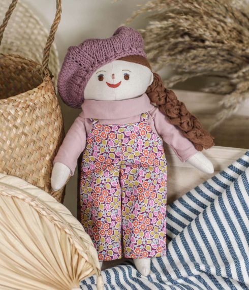 Little Lenni doll Lilly standing, dressed in a floral jumpsuit, rose turtleneck and with a knitted beret on top of her head. Organic, natural materials. Handmade soft toy.