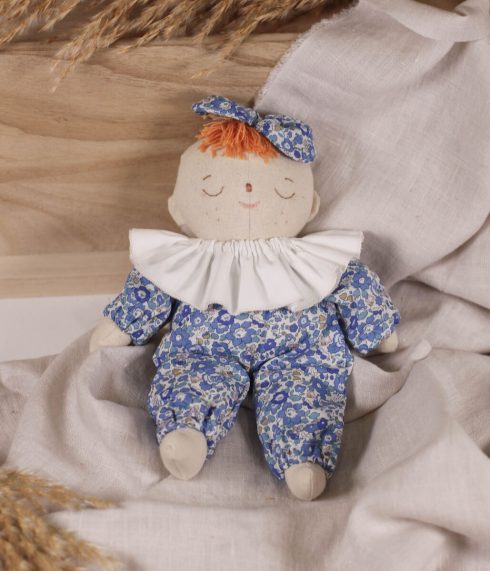 Little Lenni baby doll Liv, sleeping dressed in floral blue Liberty of London overalls and with white ruffle collar around her neck.