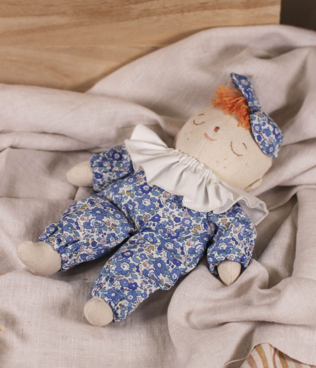 Little Lenni baby doll Liv, sleeping dressed in floral blue Liberty of London overalls and with white ruffle collar around her neck.