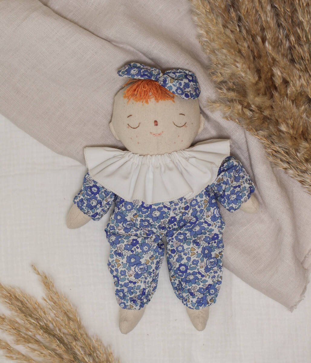 Little Lenni baby doll Liv, sleeping dressed in floral blue Liberty of London overalls and with white ruffle collar around her neck.