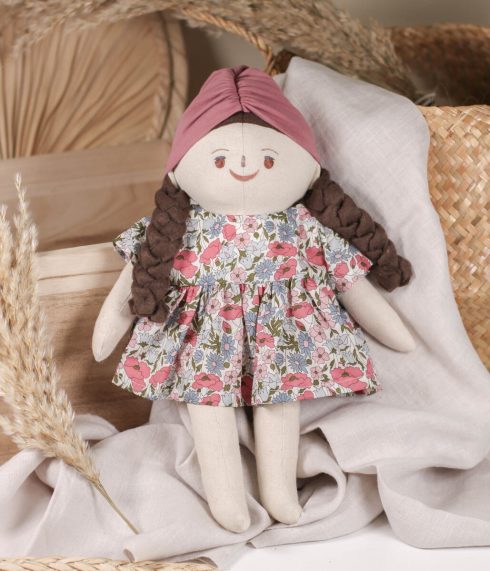 Little Lenni lutka Mila, sa pletenom tamnosmeđom kosom i očima boje lješnika, sjedi u cvjetnoj haljinici i šarenom turbanu. Ručno rađena od prirodnih i organskih materijala.