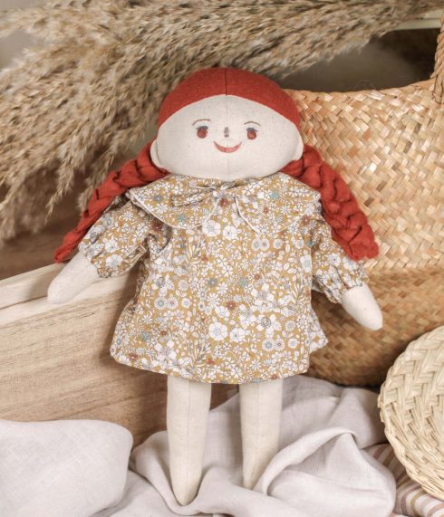 Hazelnut-eyed Little Lenni doll Olivia, with two terracotta ginger braids, standing dressed in a floral Liberty of London dress. Organic, natural materials. Handmade doll.