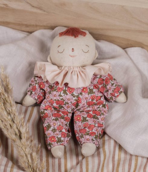 Little Lenni baby doll Poppy, sleeping dressed in floral red Liberty of London overalls and with pastel pink ruffle collar around her neck.