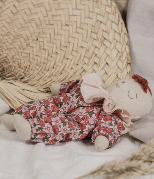 Little Lenni baby doll Poppy, sleeping dressed in floral red Liberty of London overalls and with pastel pink ruffle collar around her neck.