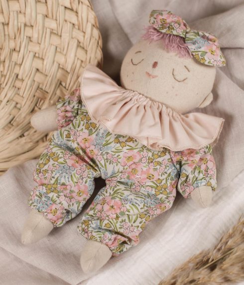 Little Lenni baby doll Rosie, sleeping dressed in floral overalls and with pastel pink ruffle collar around her neck.