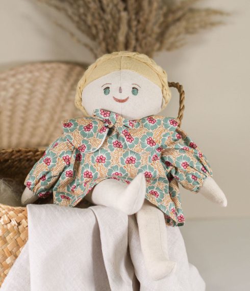 Sophie Doll, a green eyed Little Lenni doll, with blonde braided hair, sitting on a basket, dressed in a floral dress. Handmade with hand-embroidered face, made with natural organic materials.
