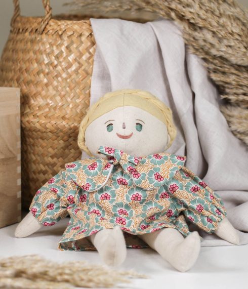 Sophie Doll, a green eyed Little Lenni doll, with blonde braided hair, sitting dressed in a floral dress. Handmade with hand-embroidered face, made with natural organic materials.